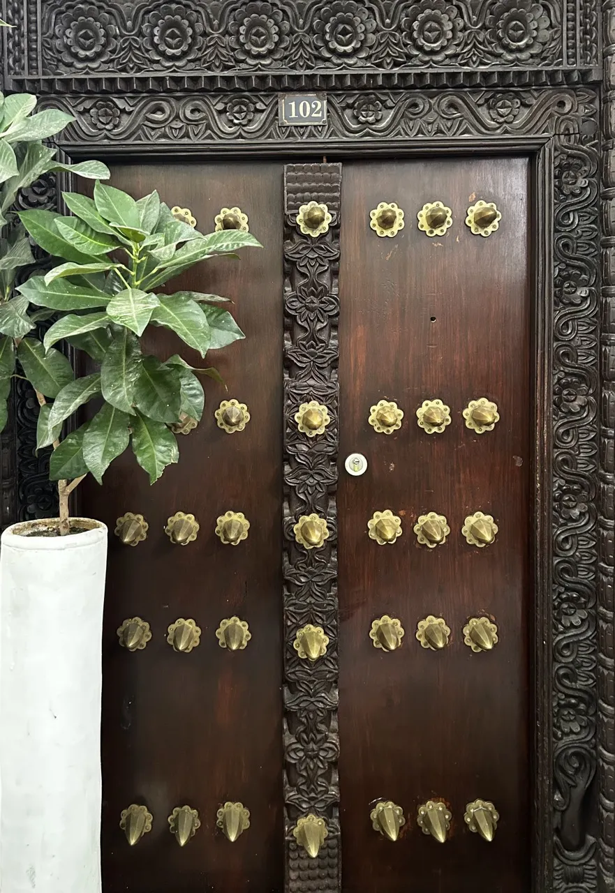 The carved wooden front door of Habari House, number 102, with brass studs
