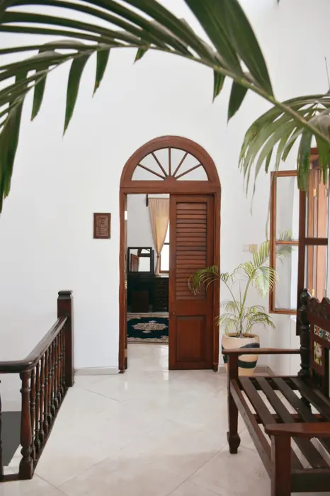 Arched louvred wooden door to a guest room, framed by palm leaves