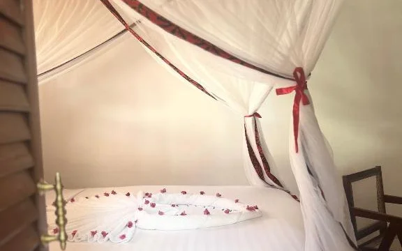 Four-poster queen bed with white linen and a ruby-red trimmed mosquito net