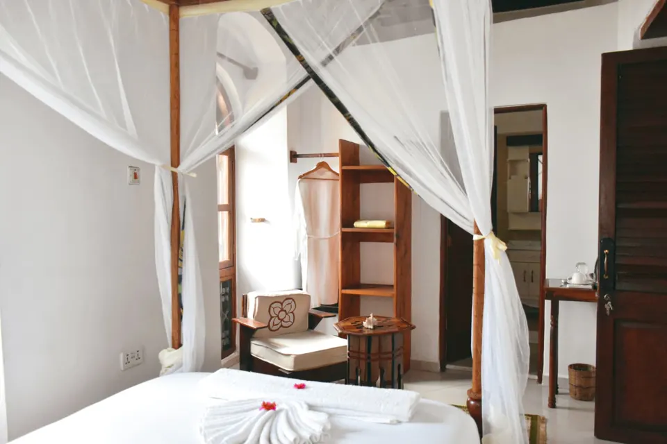 Safari Single room with a four-poster bed, reading chair and wooden shelves