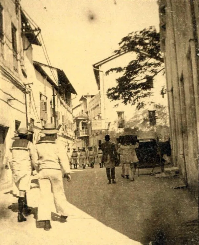 Sepia photo of sailors in white uniforms walking down a Stone Town street